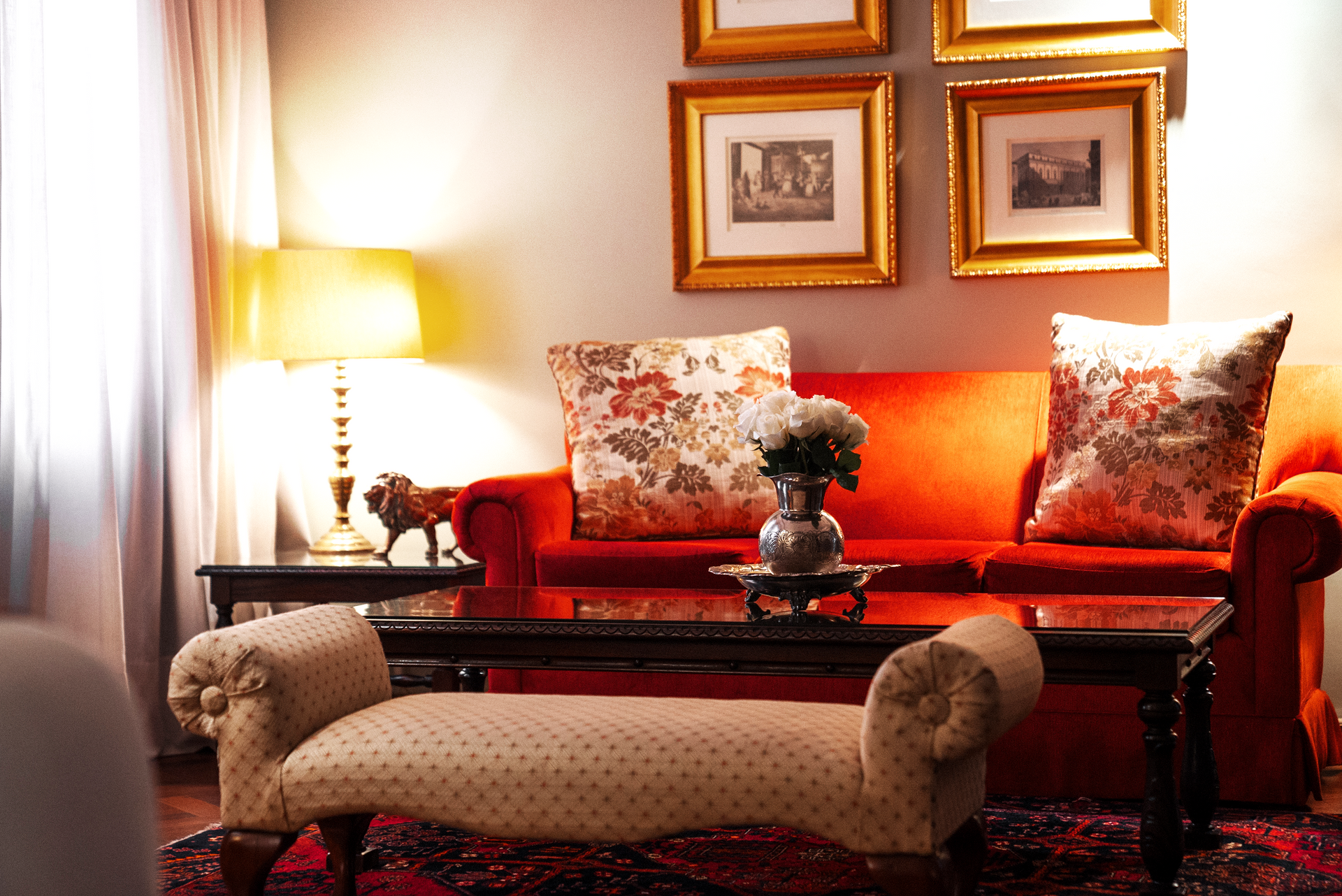 Una habitación de hotel con una cama en primer plano, una zona de estar con un sofá de color naranja brillante y suelos de madera noble con diseño de espiga.