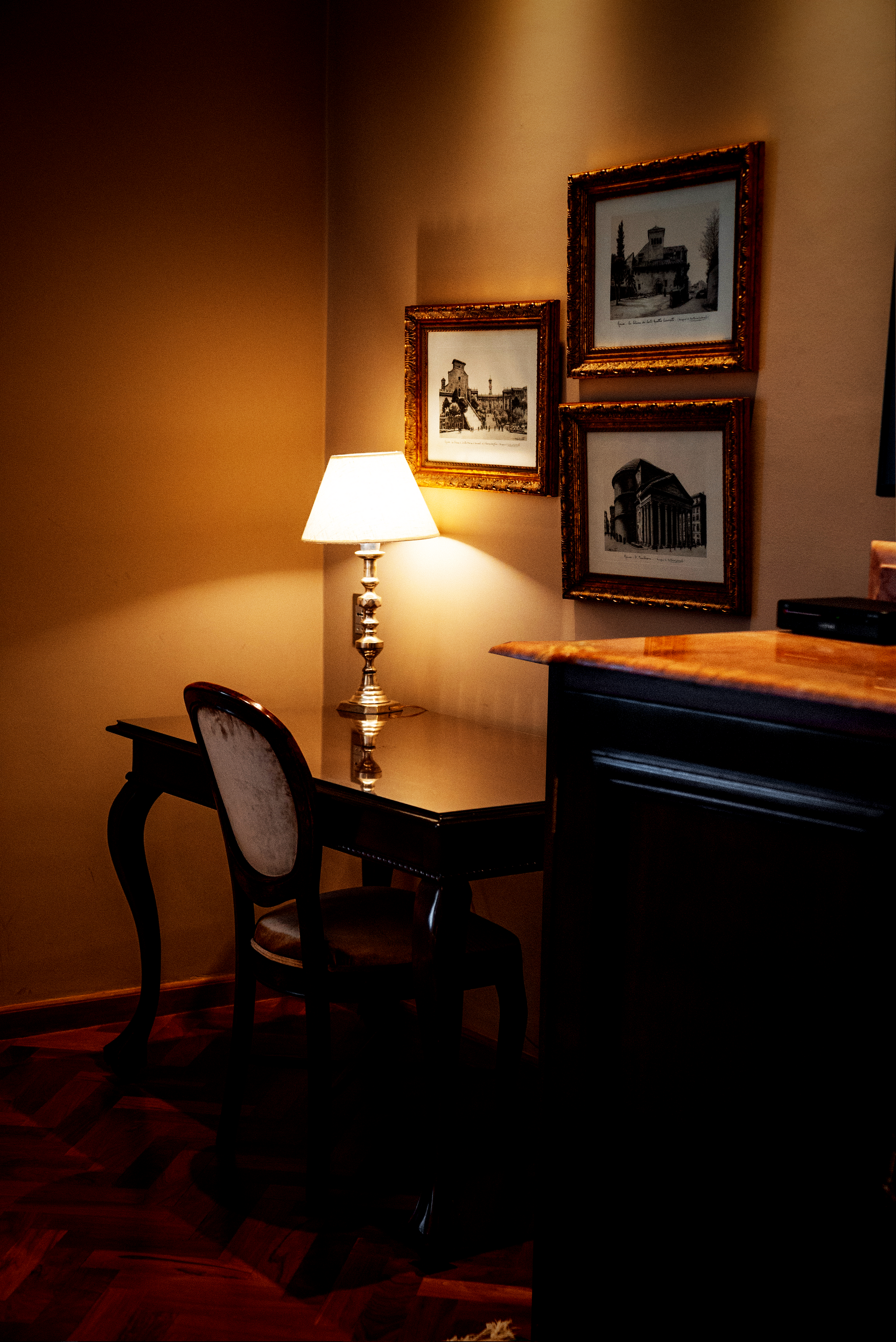 Una habitación de hotel con dos camas, un escritorio de madera con silla y lámpara, y un televisor montado en la pared sobre un armario de madera.