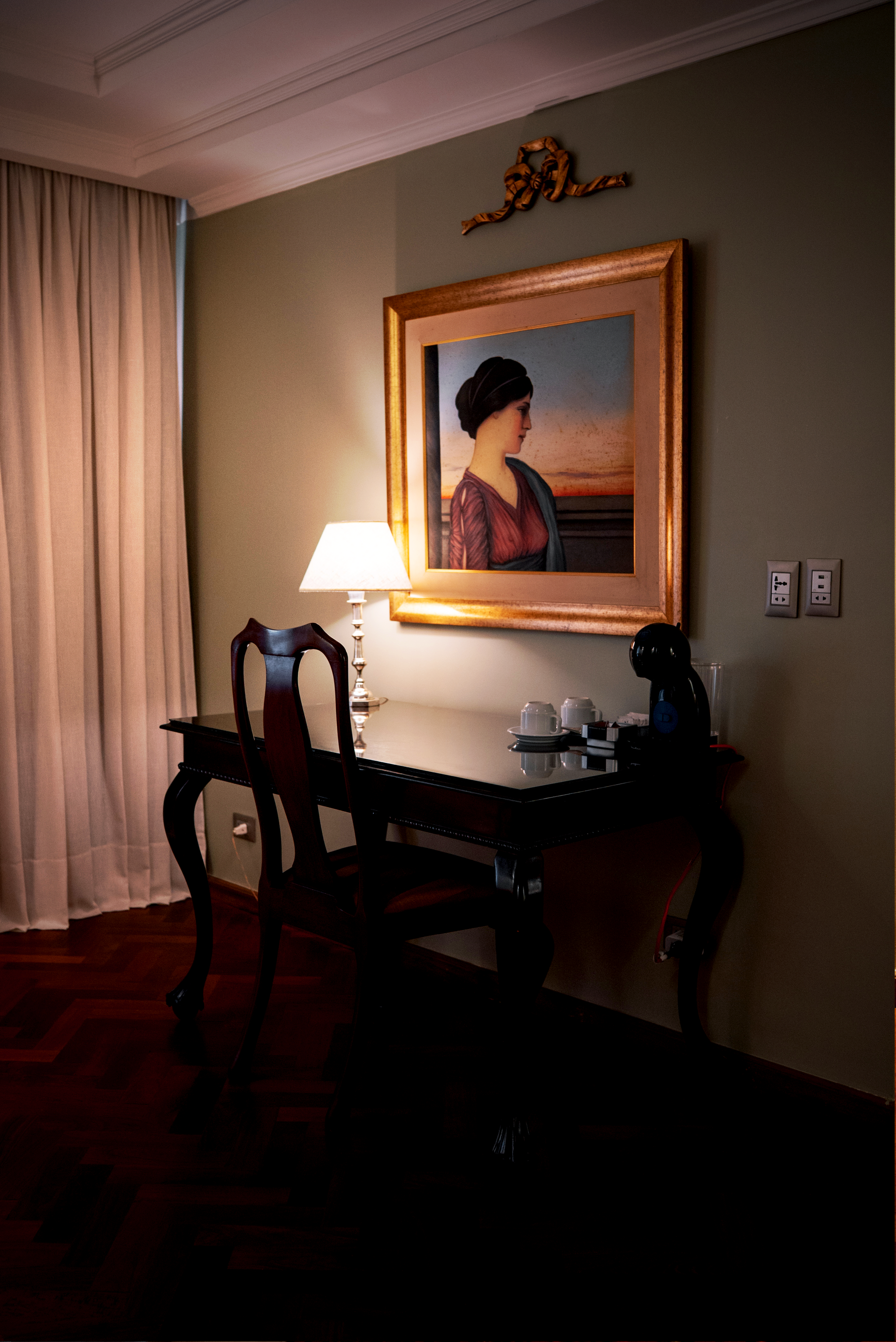 En primer plano se ve una cerradura electrónica de la puerta de un hotel, con vistas a una lujosa habitación con cama, banco y mesa de centro.