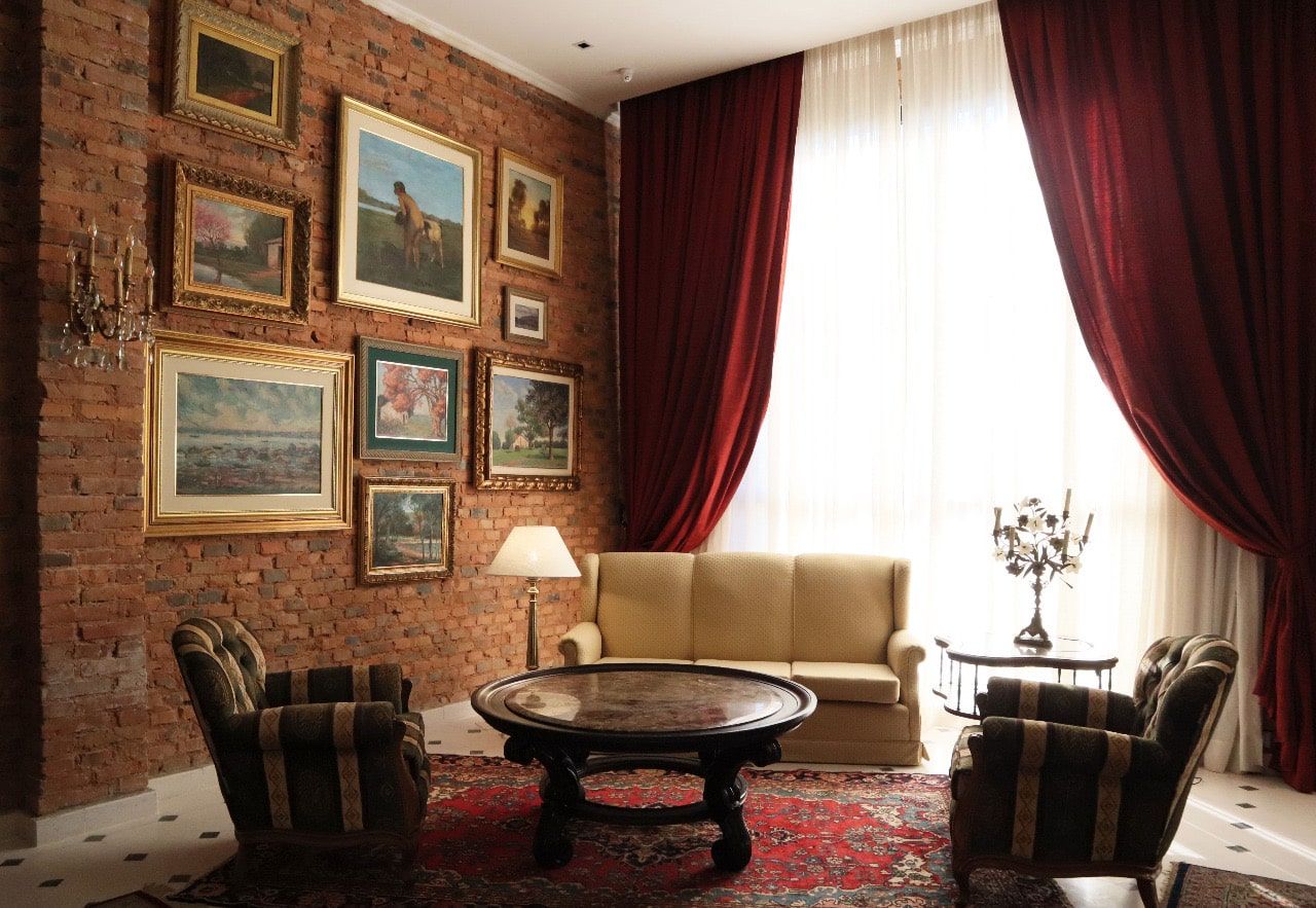 Acogedora sala de estar con pared de ladrillo, arte, sofá, sillones, cortinas rojas y mesa de café redonda.