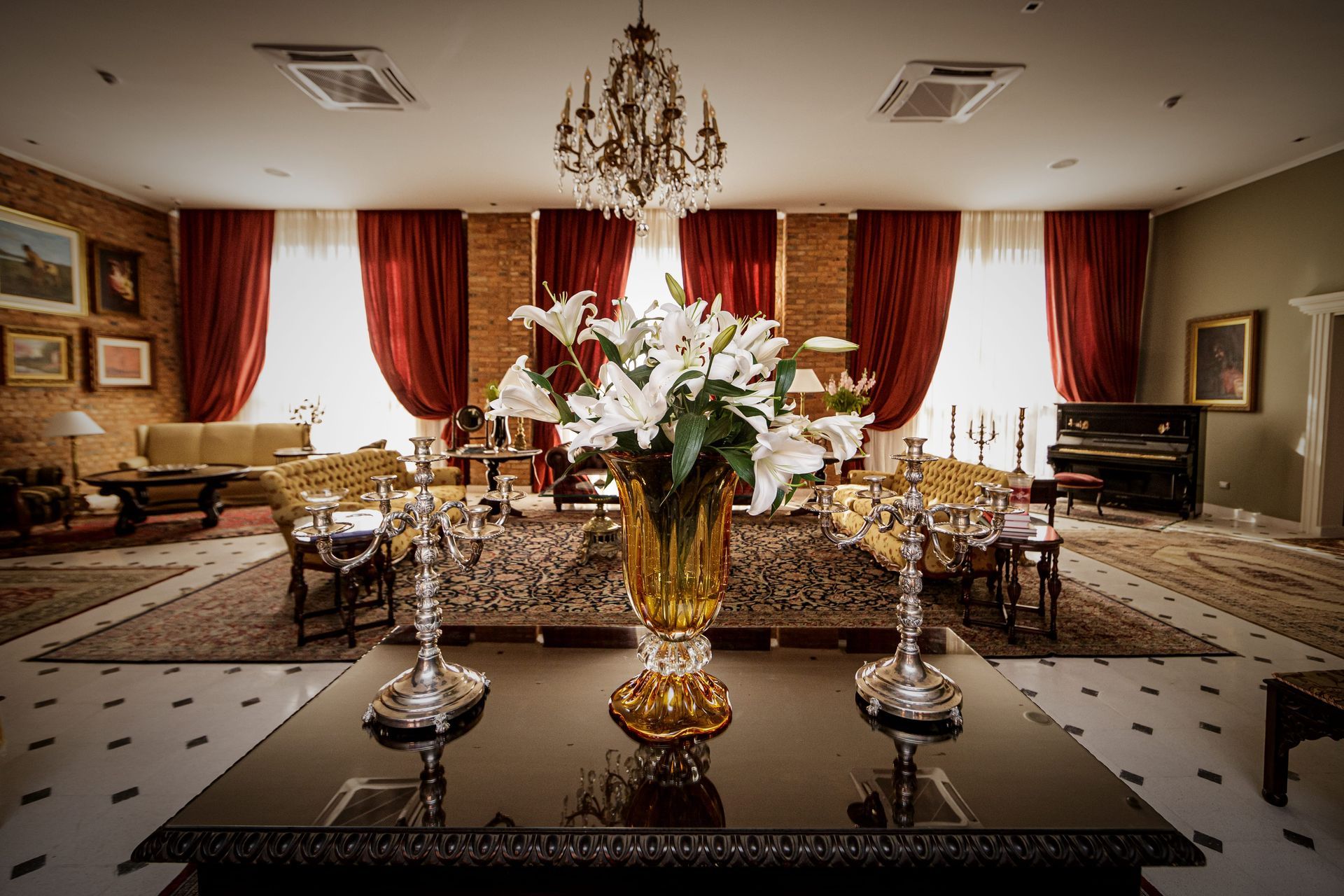 Sala de estar de lujo con flores blancas, lámpara de araña, cortinas rojas y piano de cola.