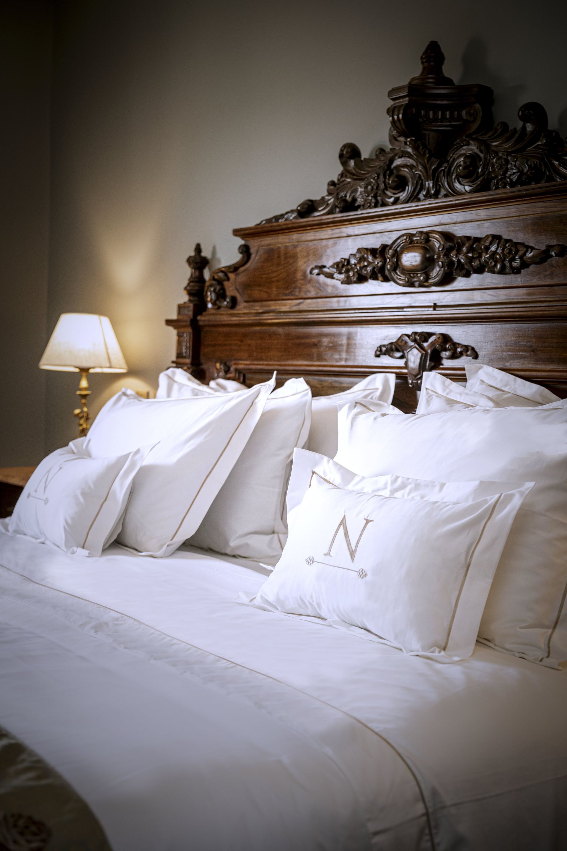 Cabecera de madera adornada con ropa de cama blanca y una almohada bordada con la letra 