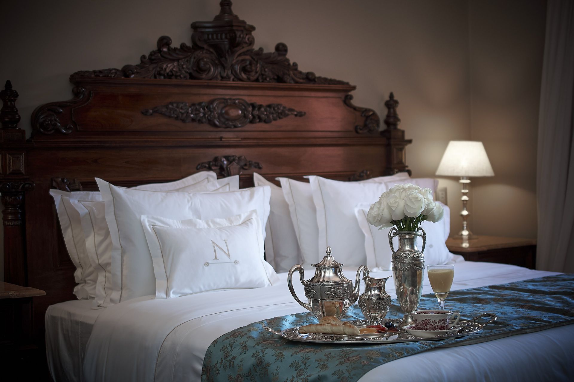 Dormitorio adornado con una bandeja de desayuno en la cama, con flores, una tetera y una bebida.