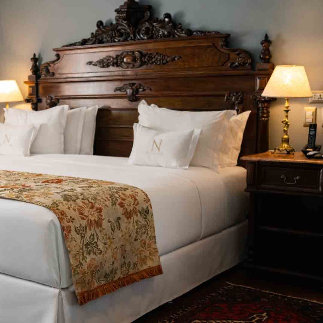 Dormitorio adornado con una cama cubierta con almohadas blancas, una bandeja de plata con juego de té y flores.