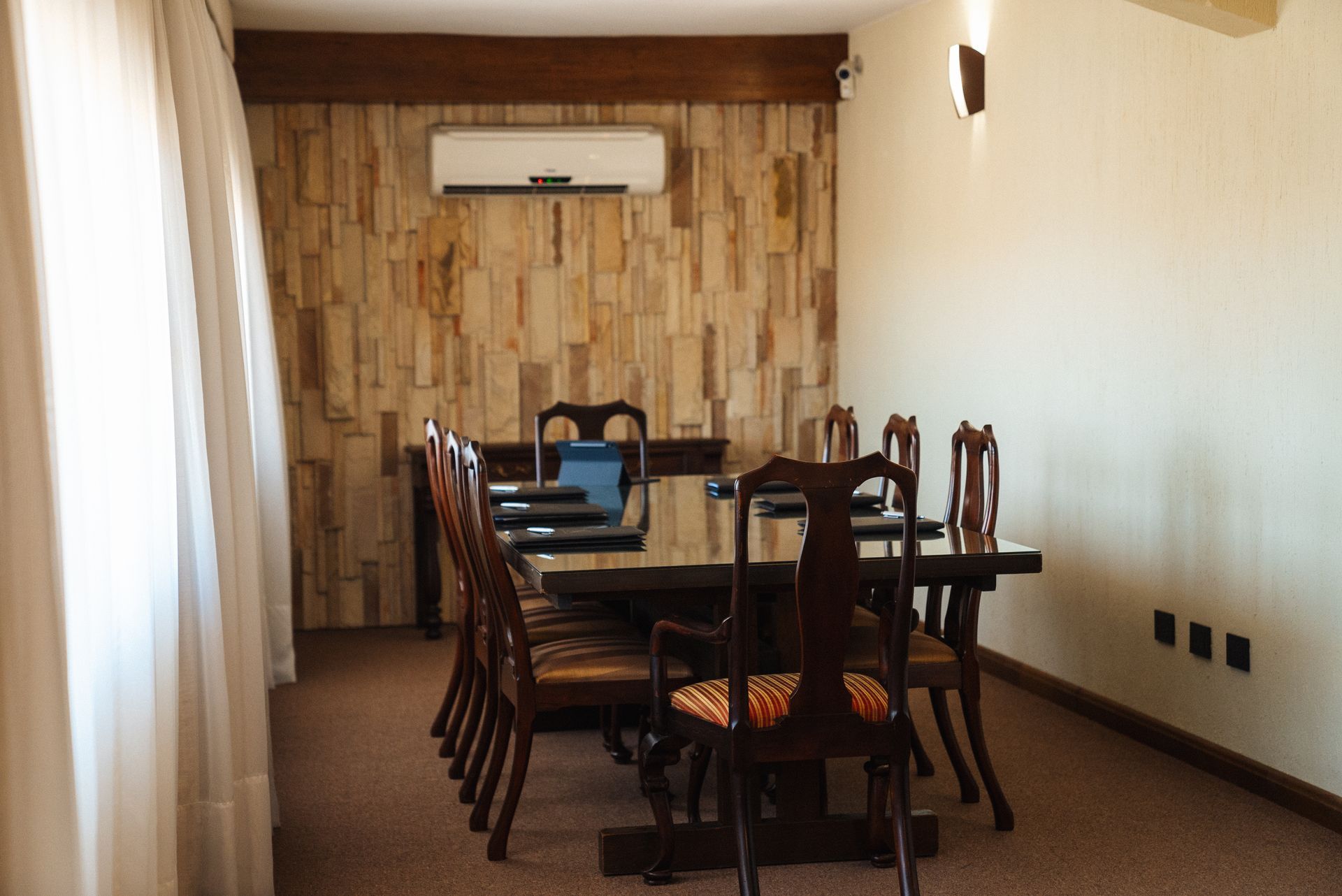 Una sala de conferencias con una gran mesa de madera, sillas, papel pintado con textura de piedra y aire acondicionado.