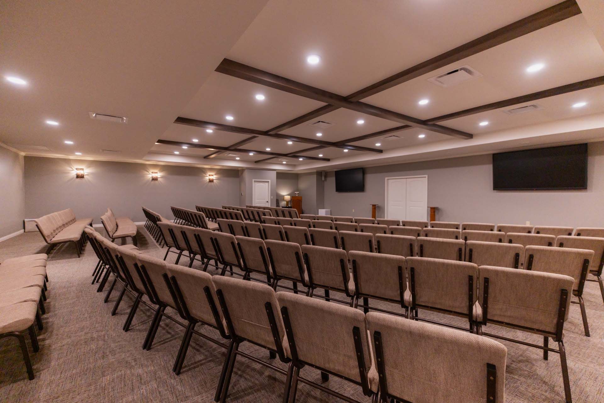 a large auditorium with rows of chairs and a television on the wall .