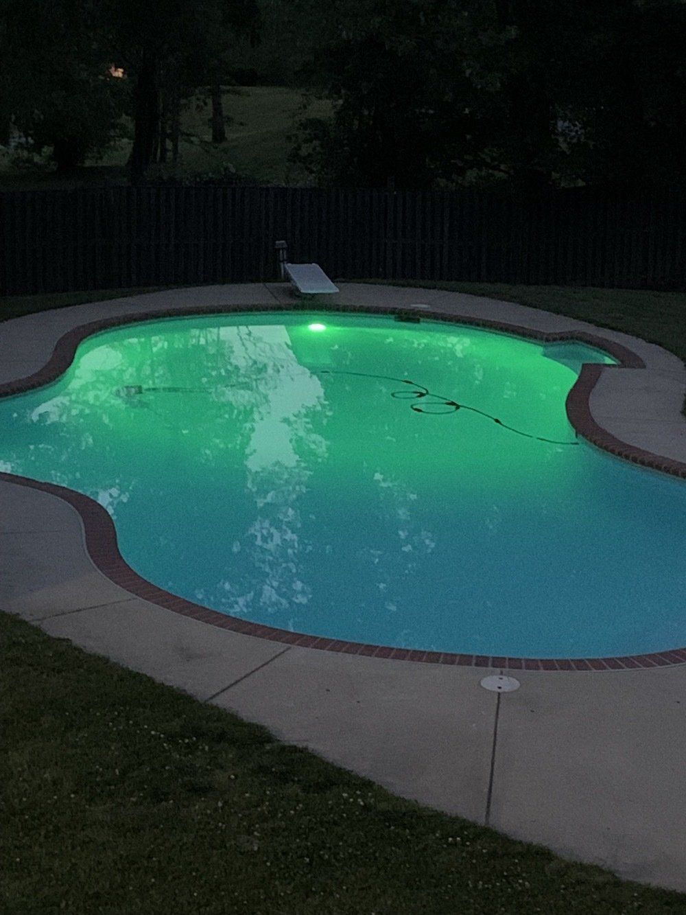 A large swimming pool is lit up at night with green lights.
