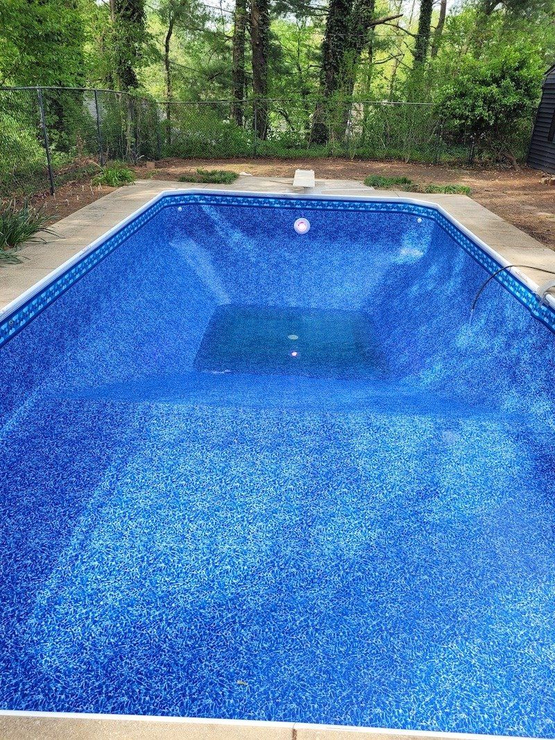A large blue swimming pool surrounded by trees in a backyard.