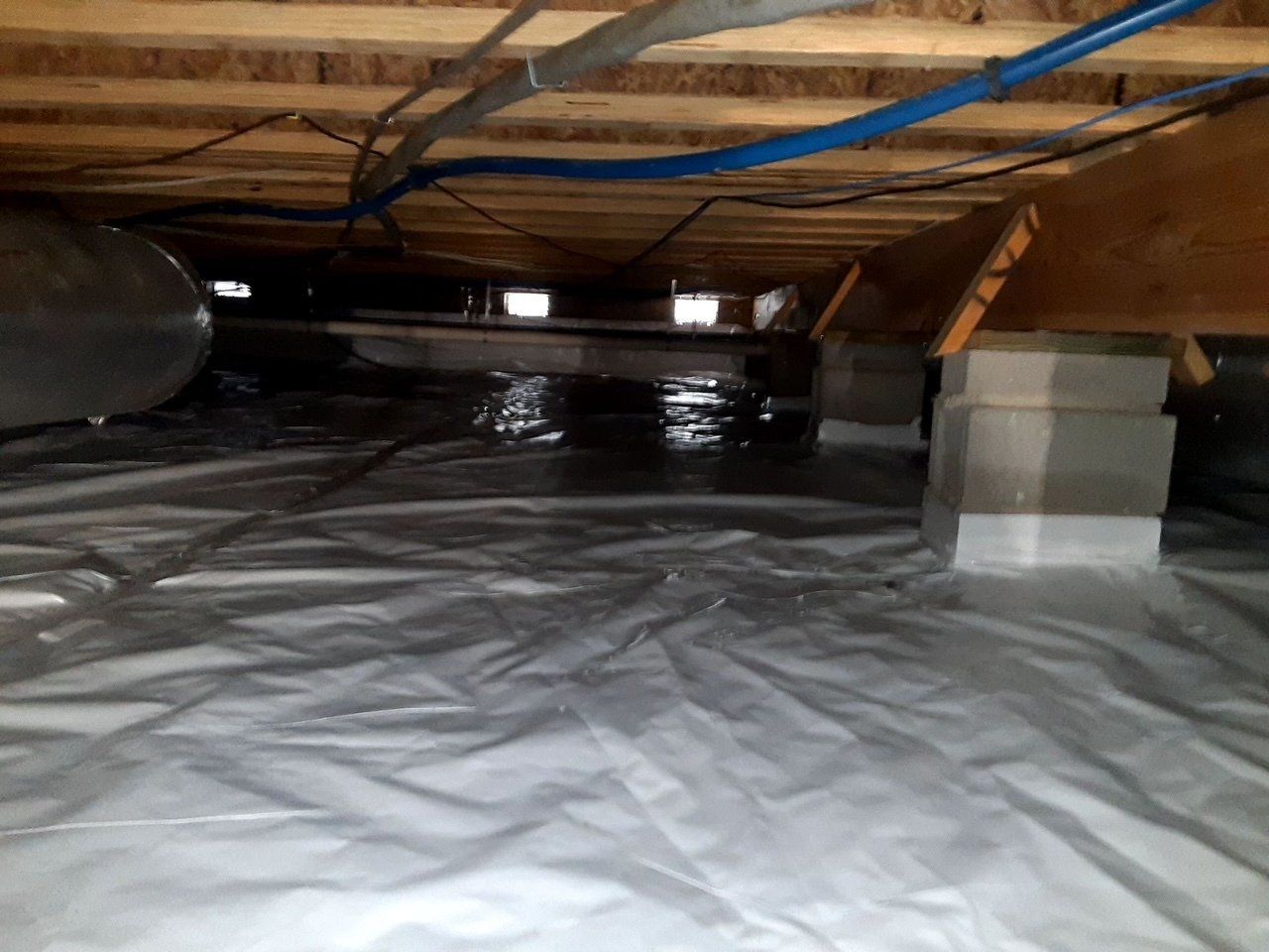 A crawl space with a lot of pipes and wires.