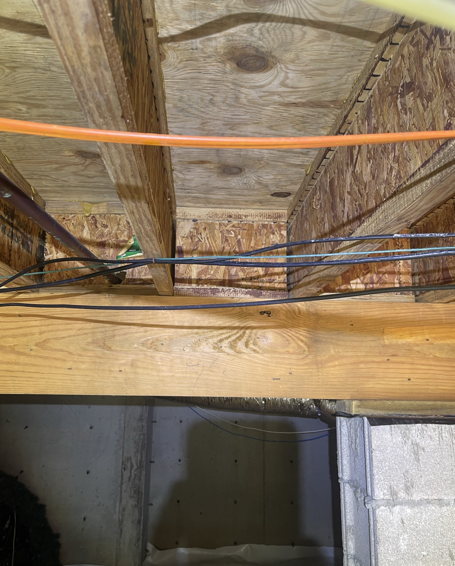 A bunch of wires are hanging from the ceiling of a basement.