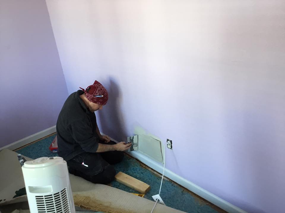 A man is kneeling on the floor working on a wall.