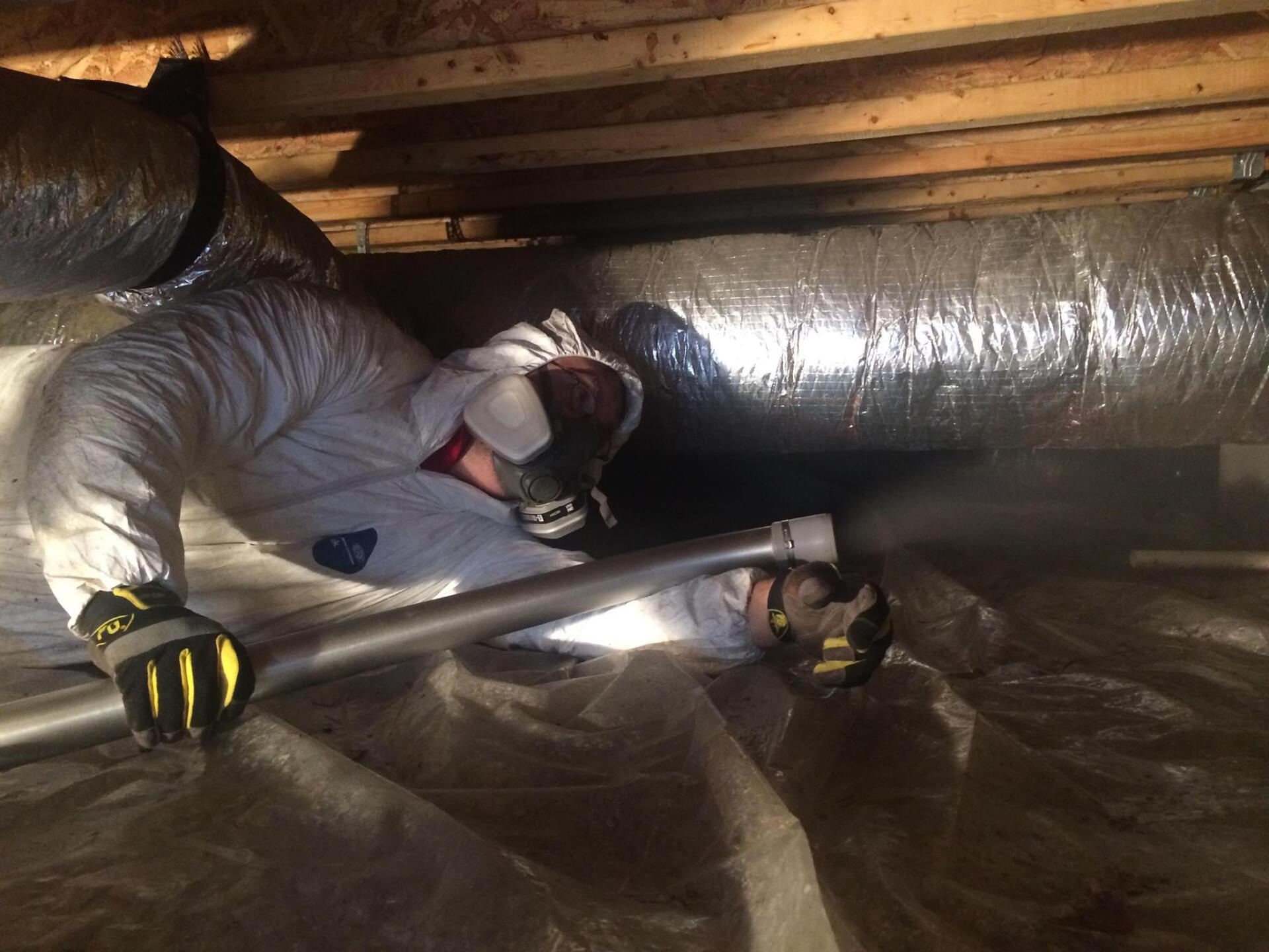 A man in a white suit is working on a duct in a basement.