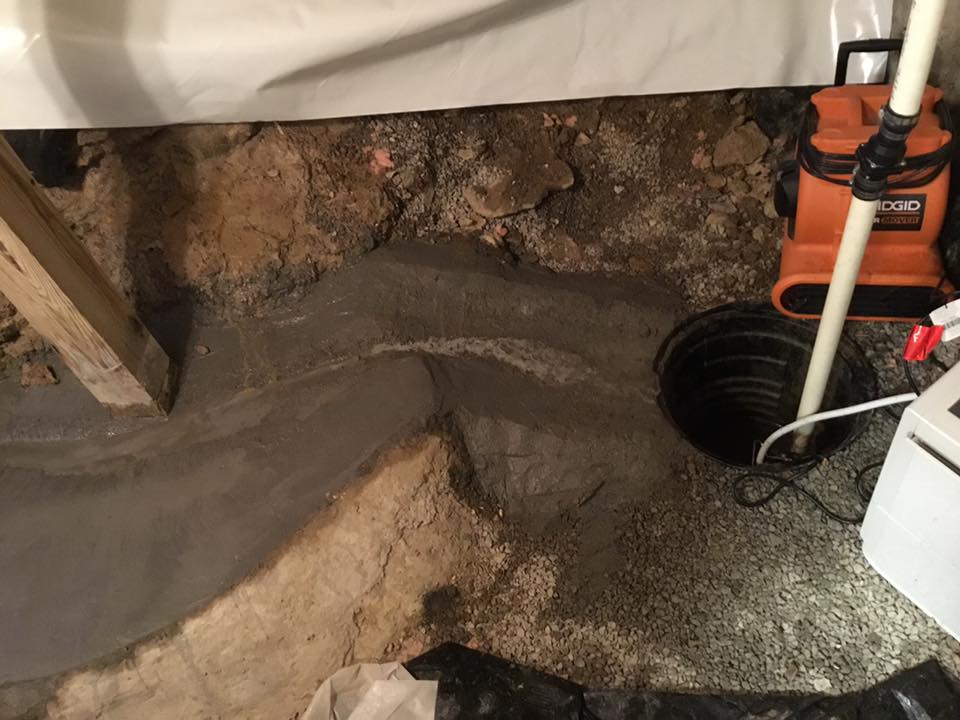 A hole in the ground in a basement with a pump in it