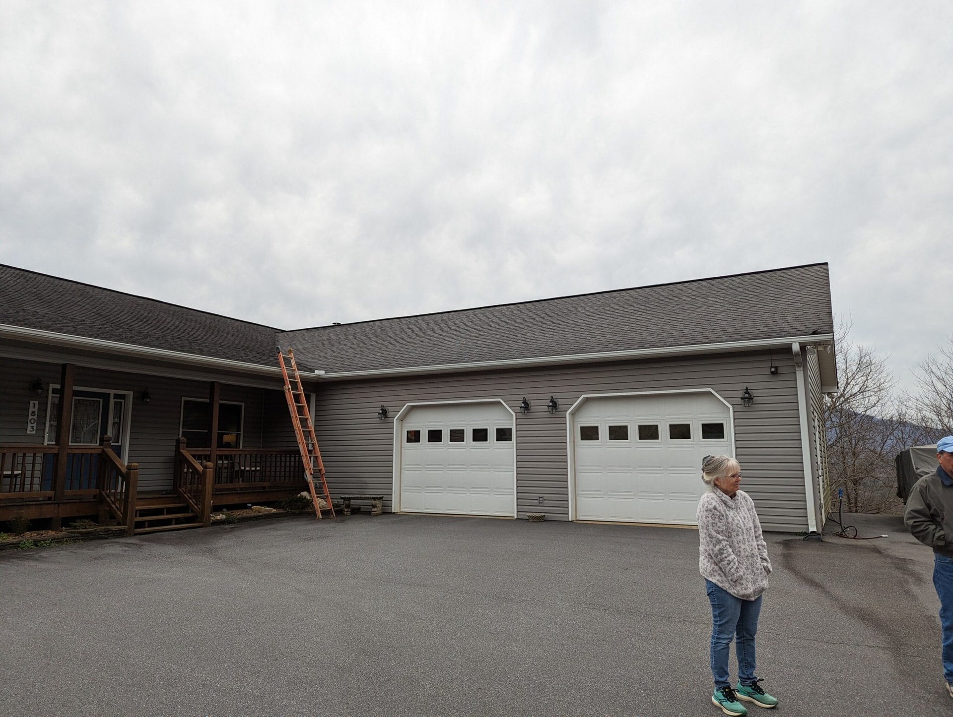 Gray house with two-car garage. A person stands in front. Cloudy sky.