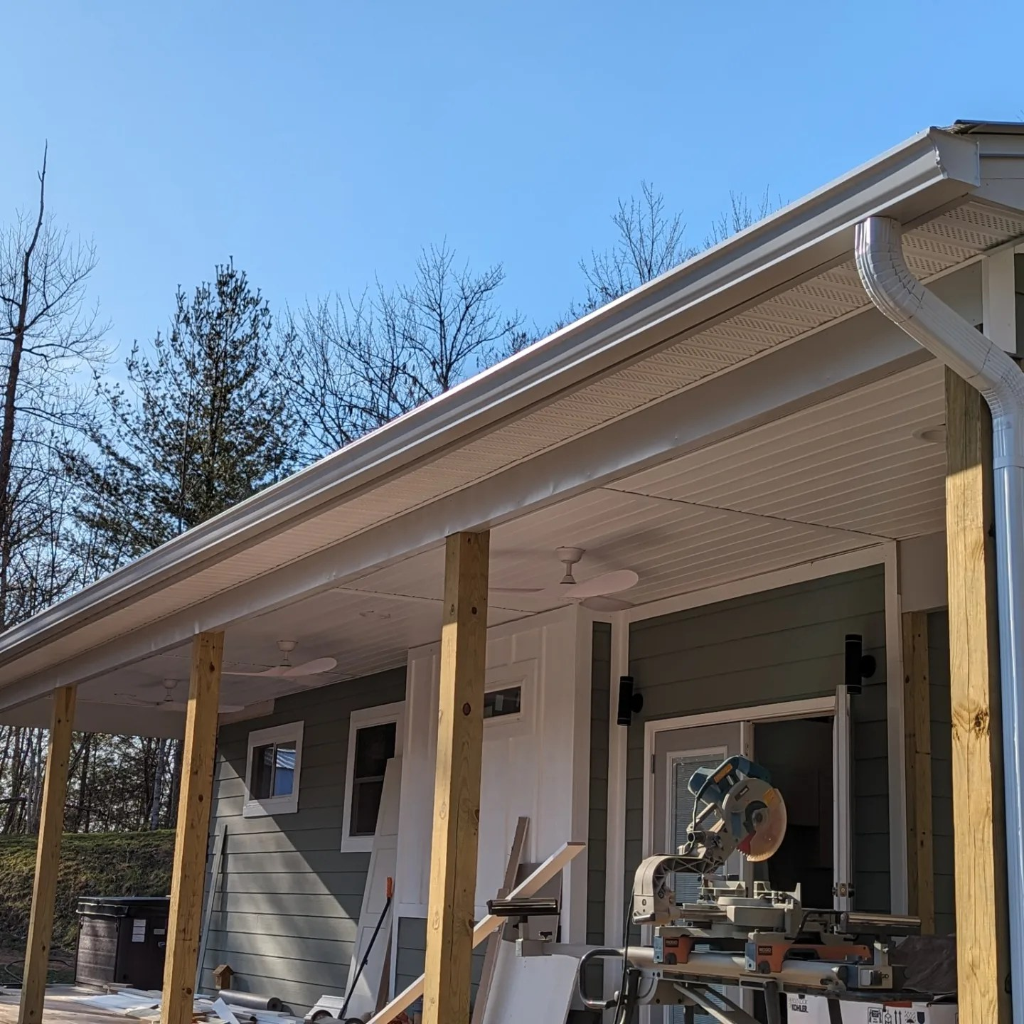 Green building with white trim, covered porch, and a miter saw.