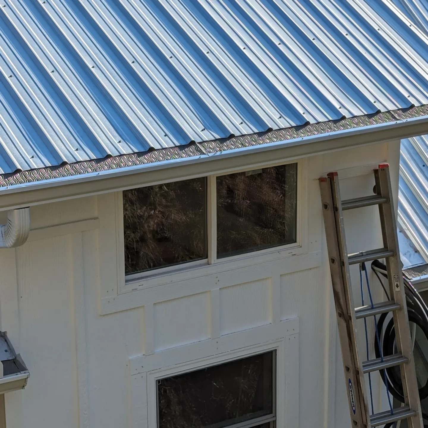 White house with a metal roof and a ladder propped up against it.