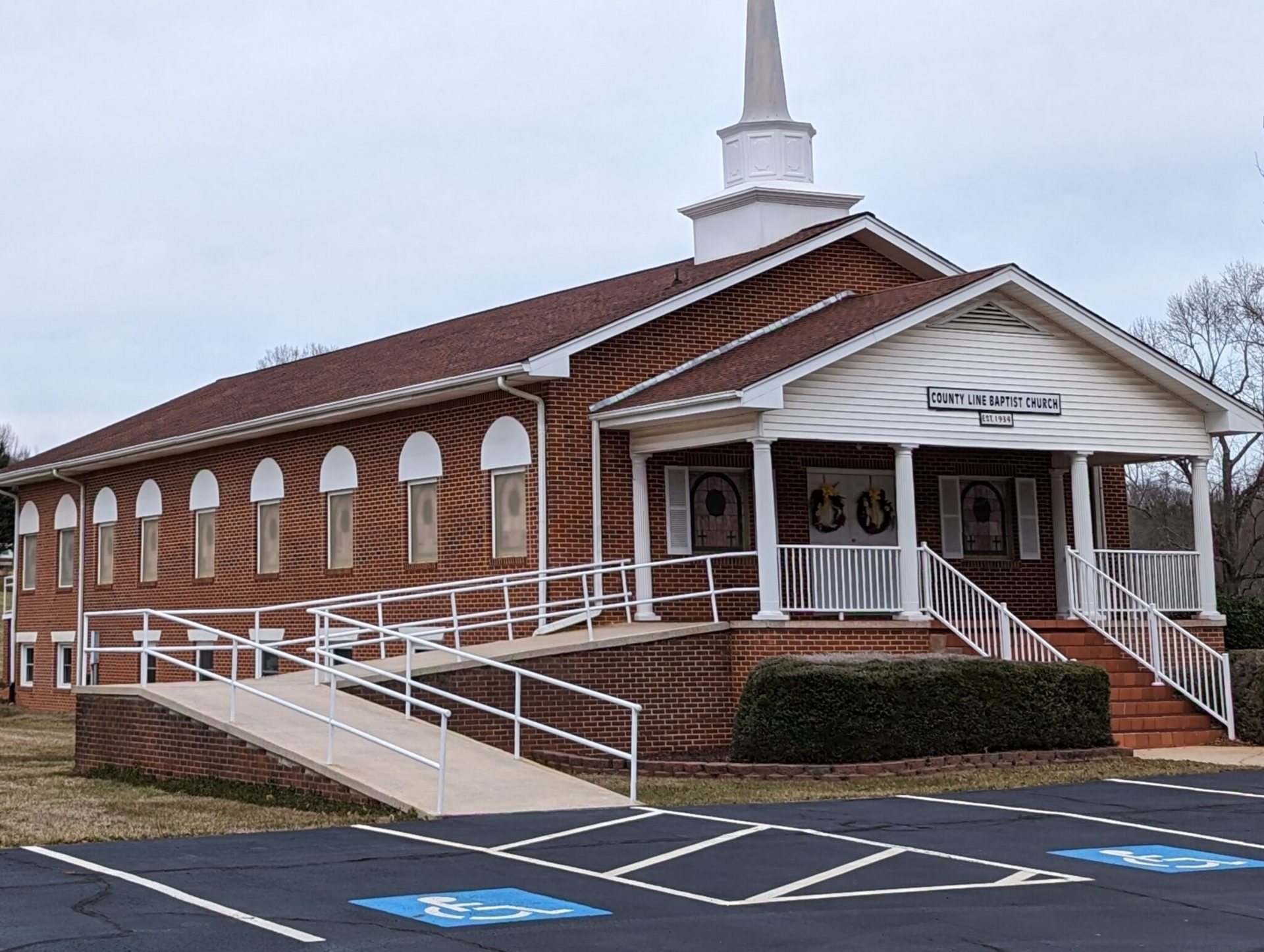 Brick church building with a white steeple, porch, and a wheelchair ramp.