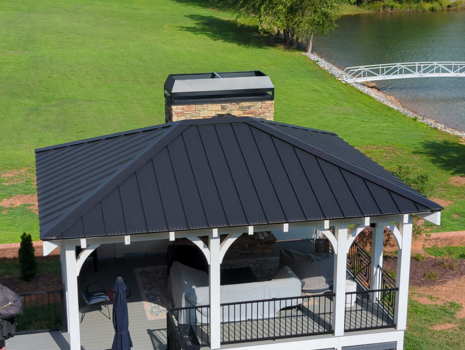 Black metal roof on a white gazebo with fireplace, lakeside setting.