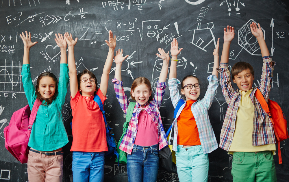 A group of children are standing in front of a blackboard with their hands in the air.