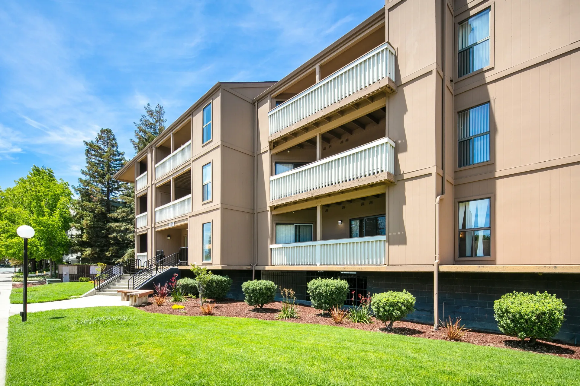 Exterior of a tan apartment building with multiple balconies and green lawn in front.