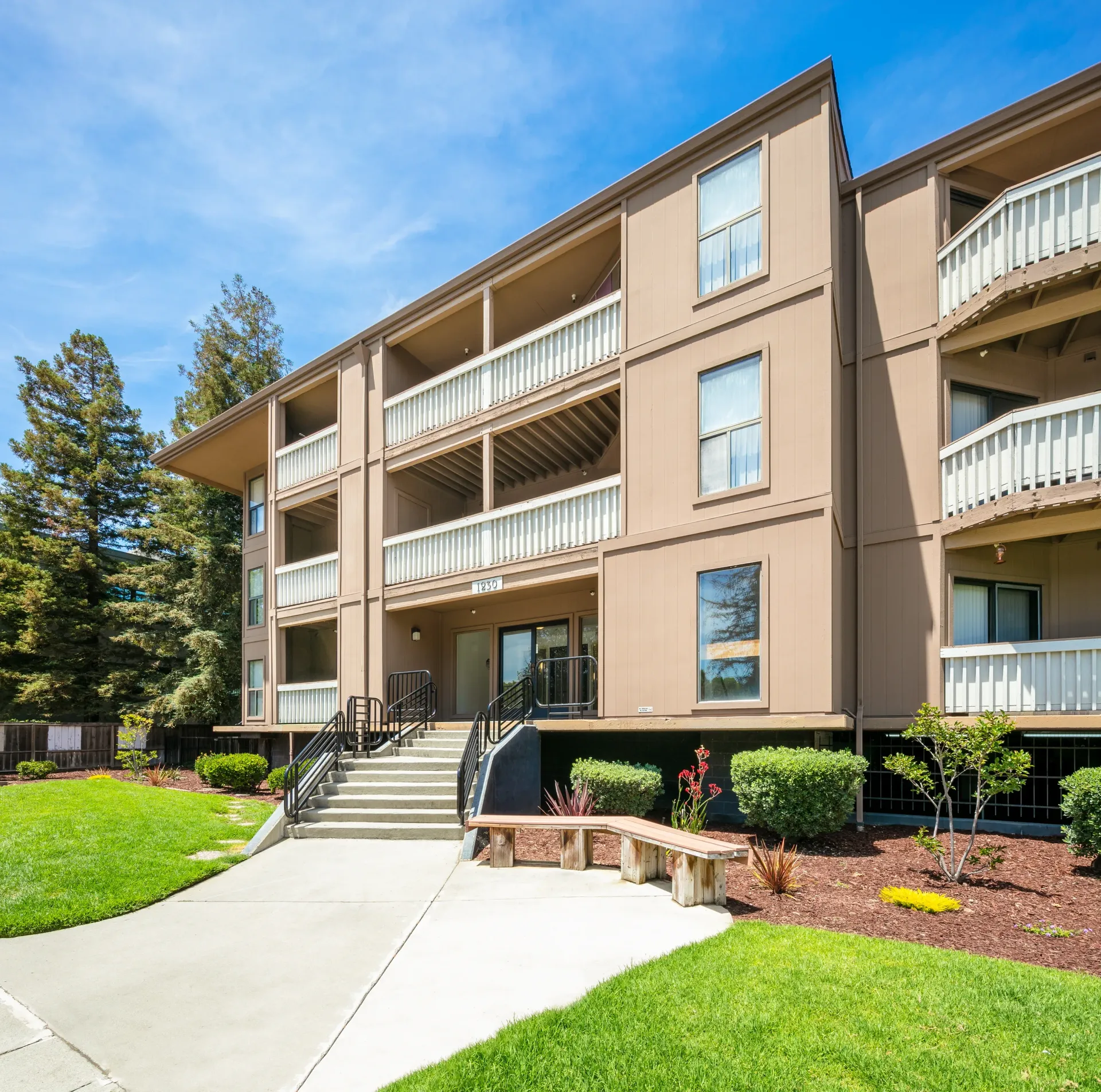 Exterior view of apartment building with balconies, manicured lawn and entrance.
