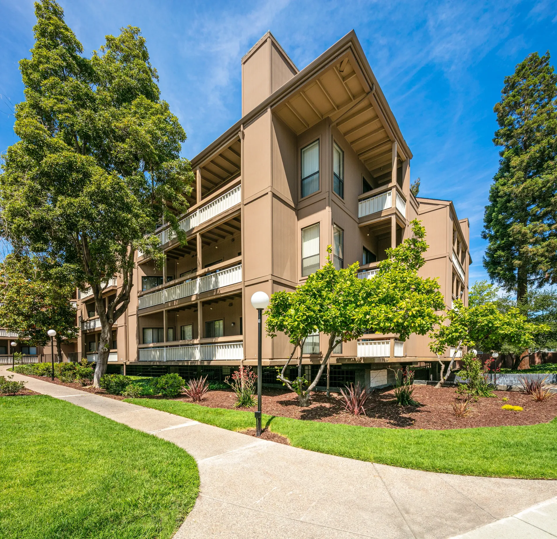 Exterior view of a tan apartment building with balconies and surrounding greenery.