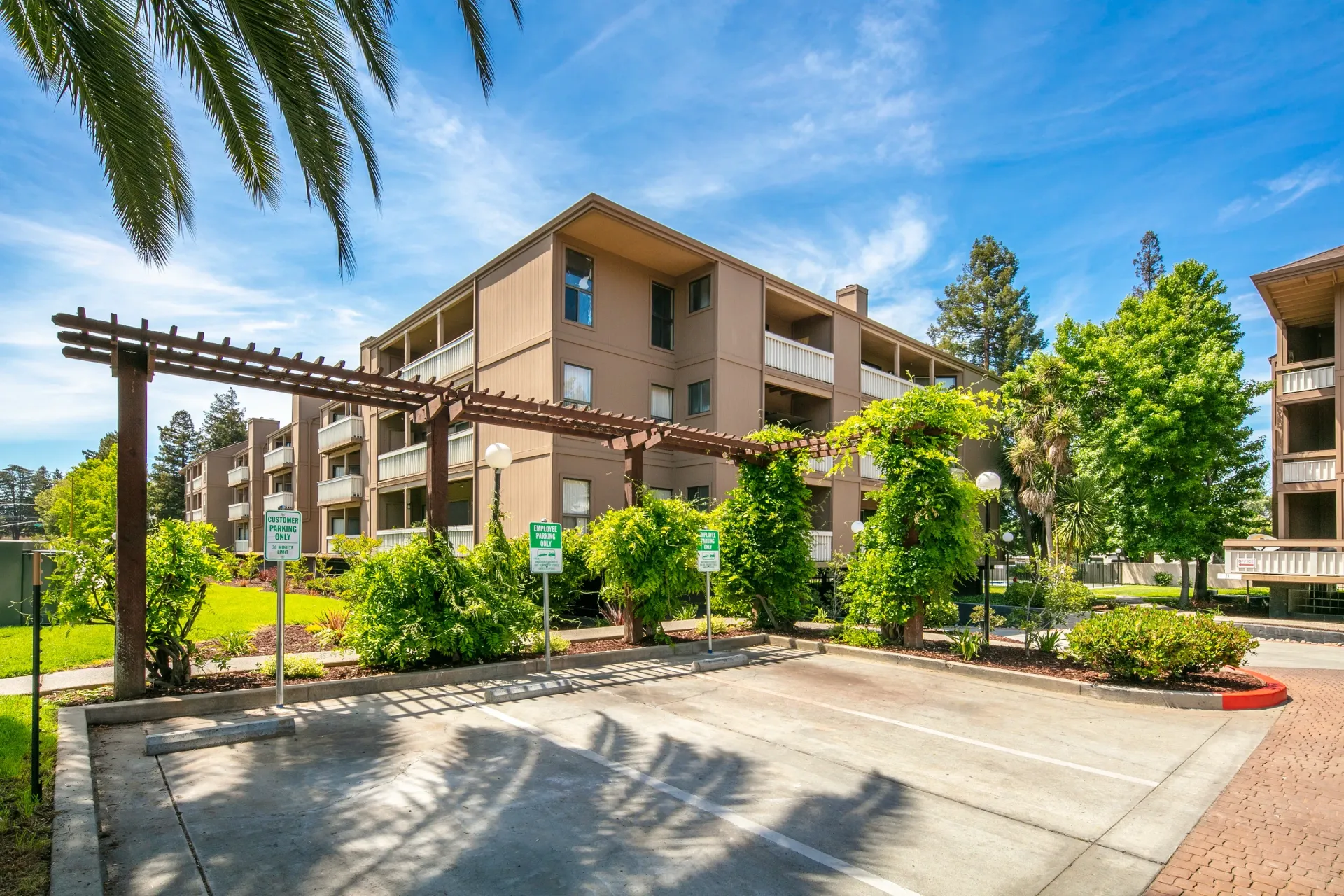 Apartment building exterior with a wooden trellis and parking lot.