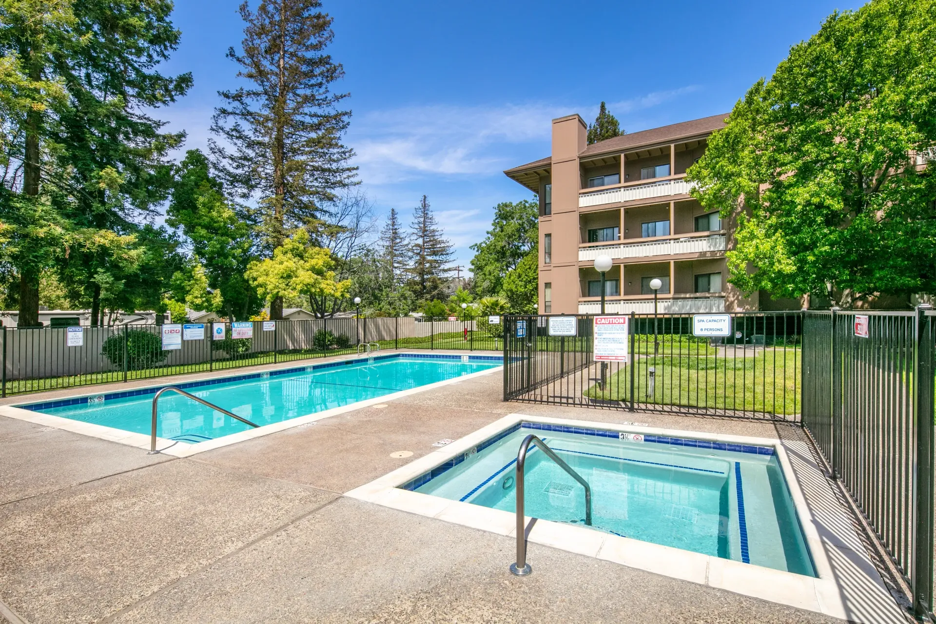 Swimming pool and spa area with surrounding trees and apartment building.