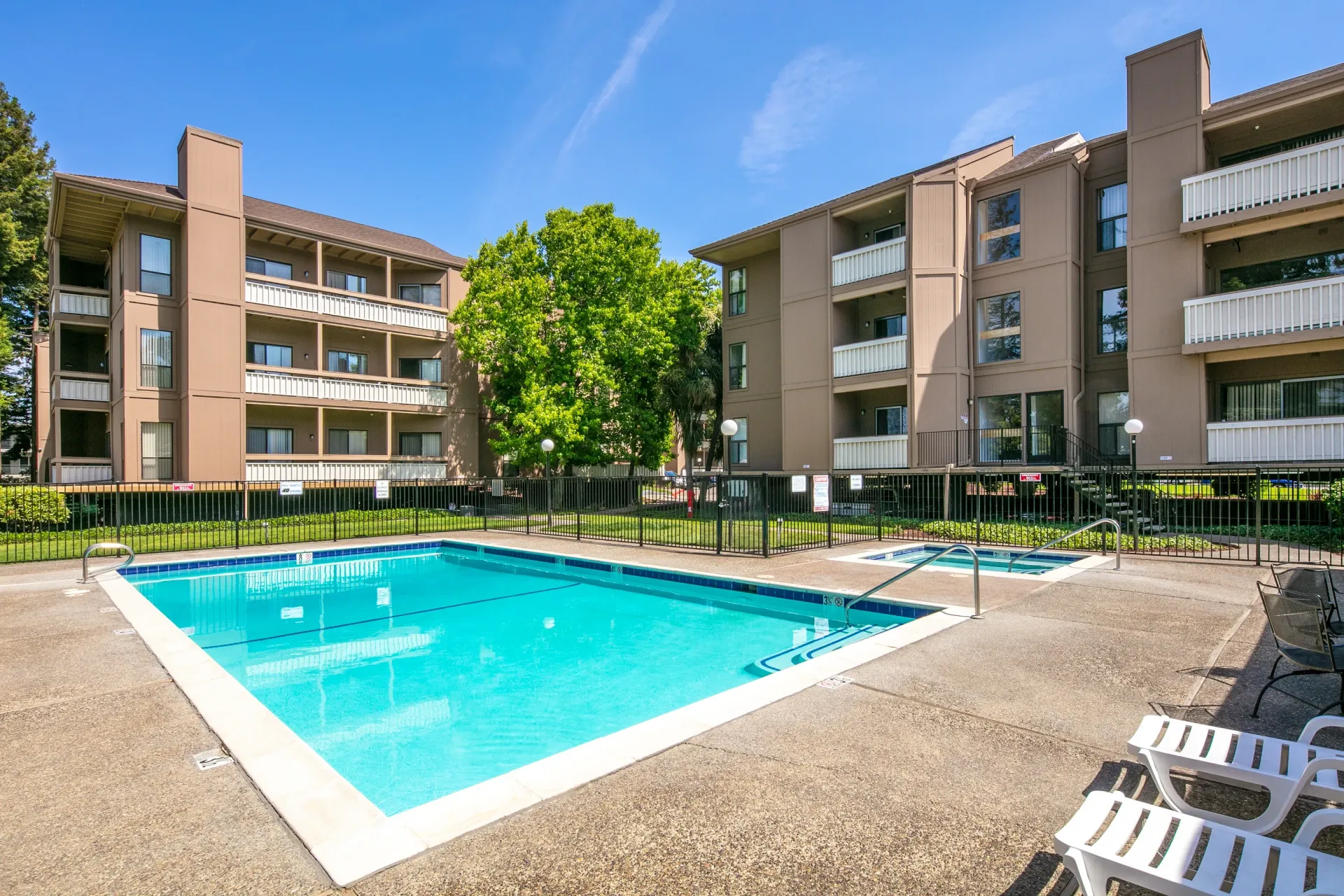 Resort-style outdoor swimming pool and spa with lounge chairs and apartment buildings in the background.