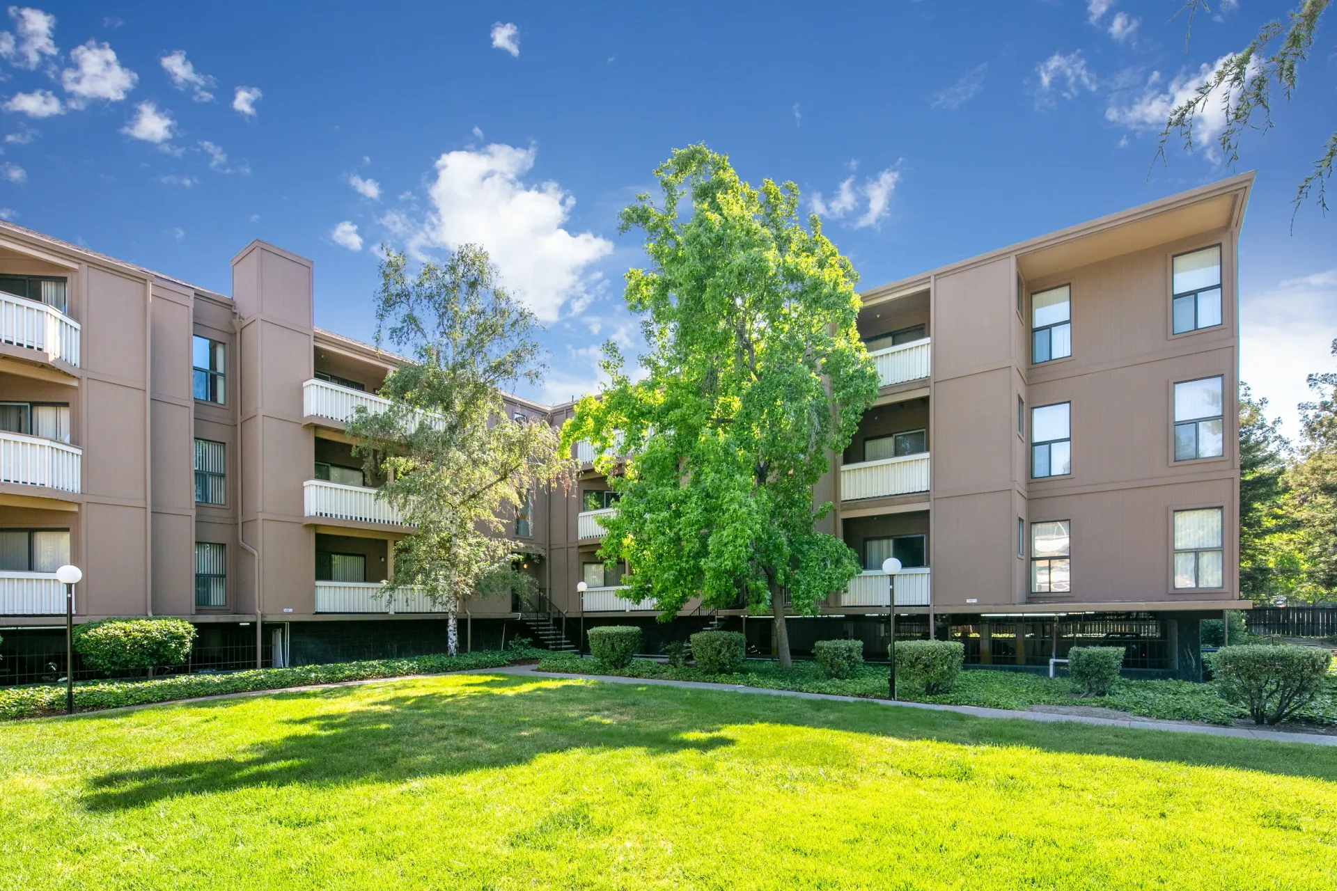 Exterior view of a multifamily building with balconies and lush green lawn.