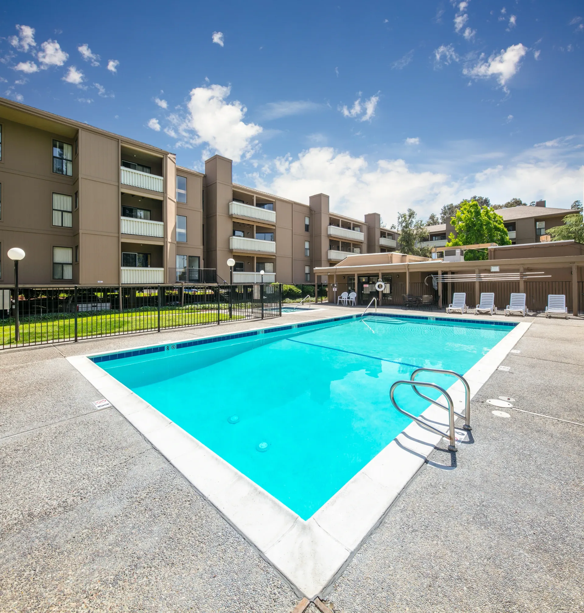 Swimming pool with lounge chairs and apartment buildings in the background.