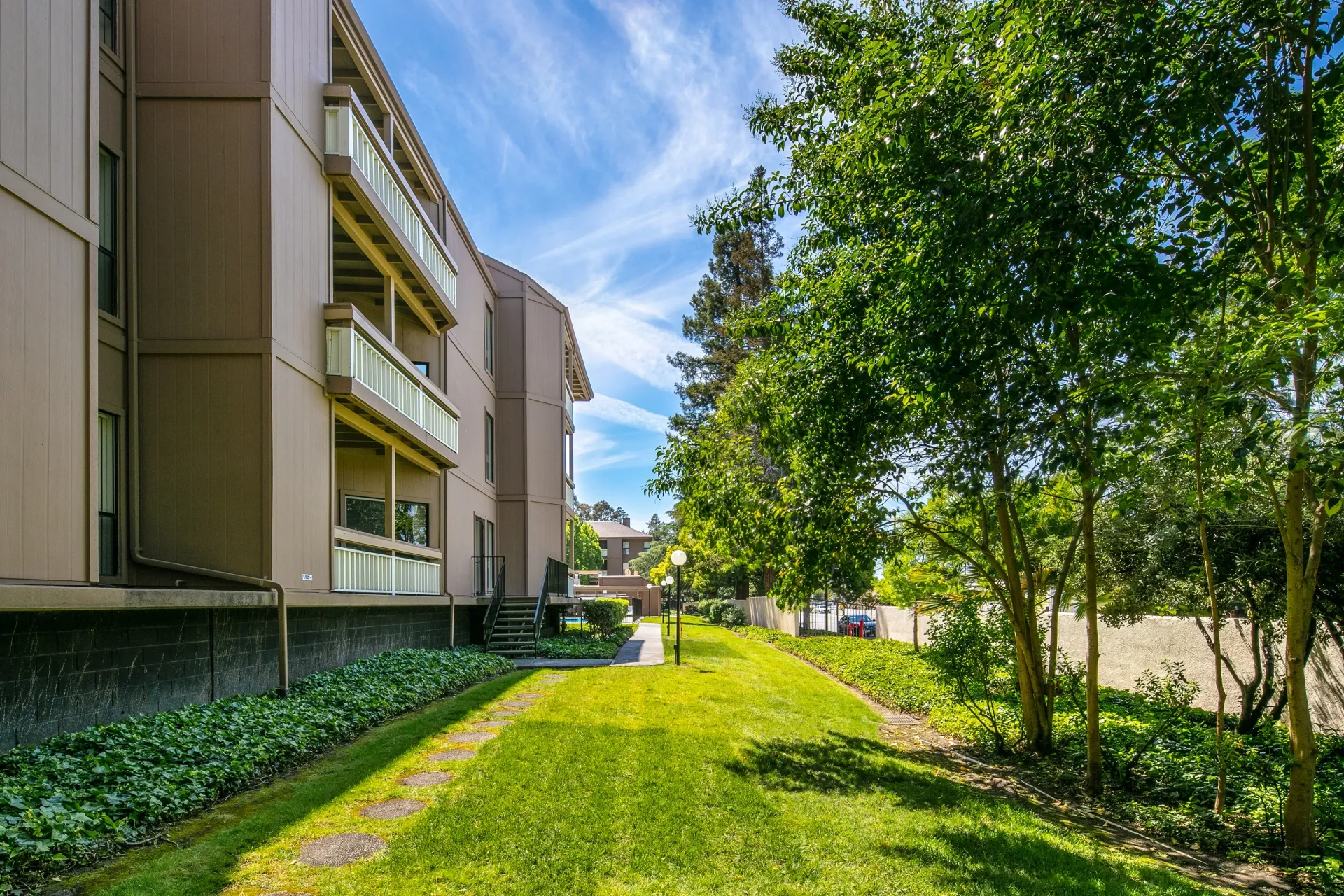 Exterior view of apartment buildings with balconies, lush green lawn, and trees.