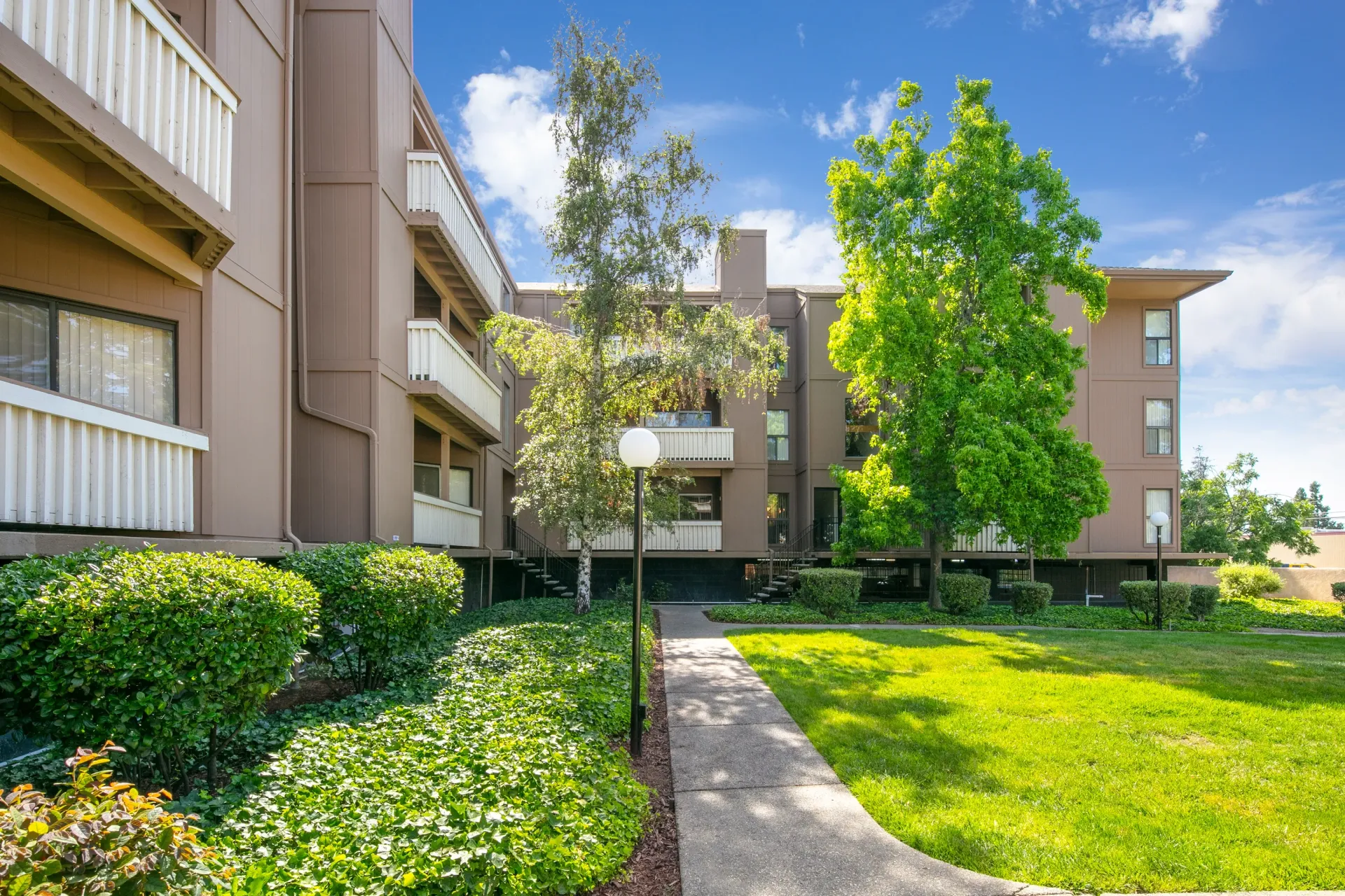 Exterior view of apartment buildings with lush landscaping and a paved walkway.