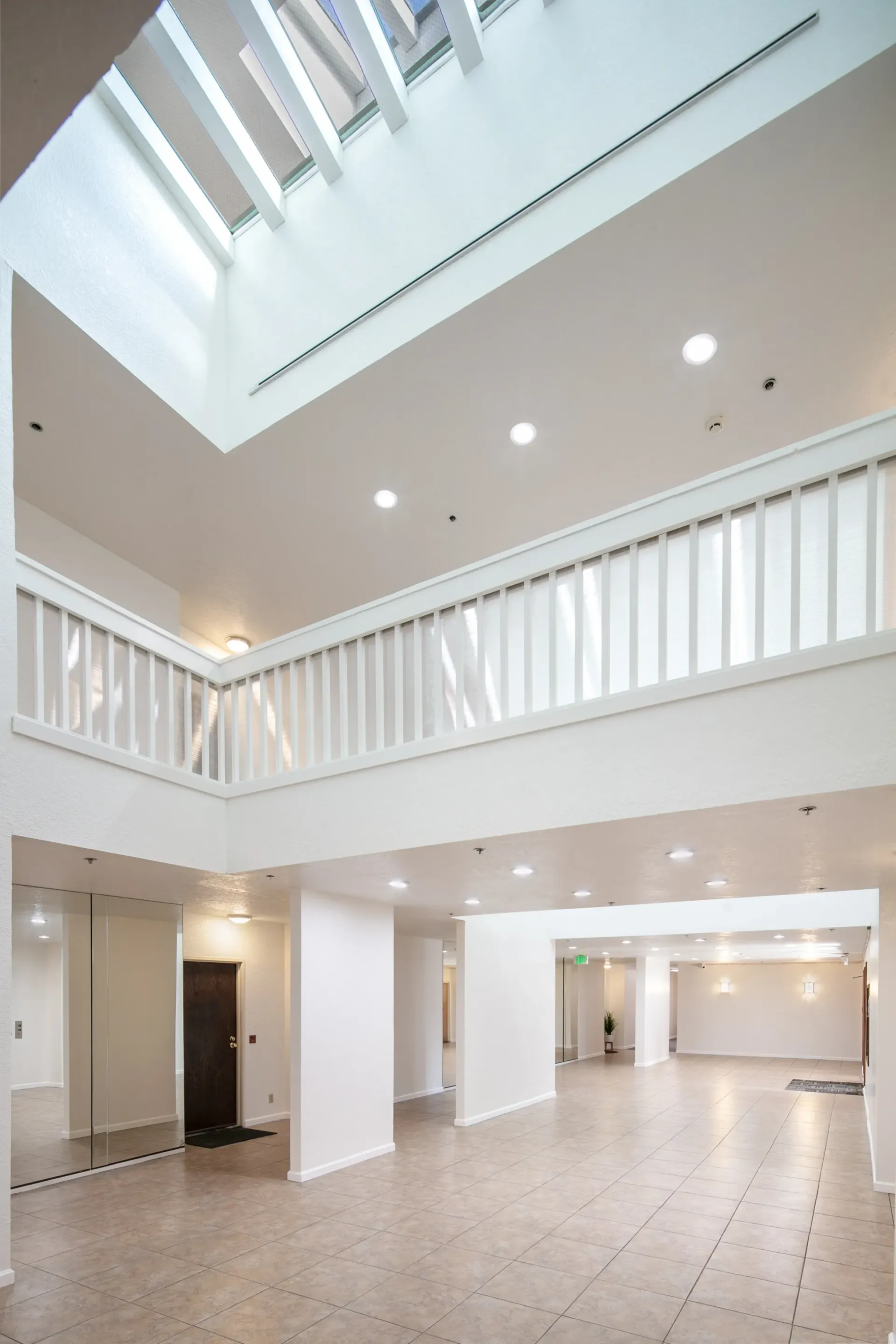 Interior view of a brightly lit, modern apartment building lobby with a skylight and upper balcony.