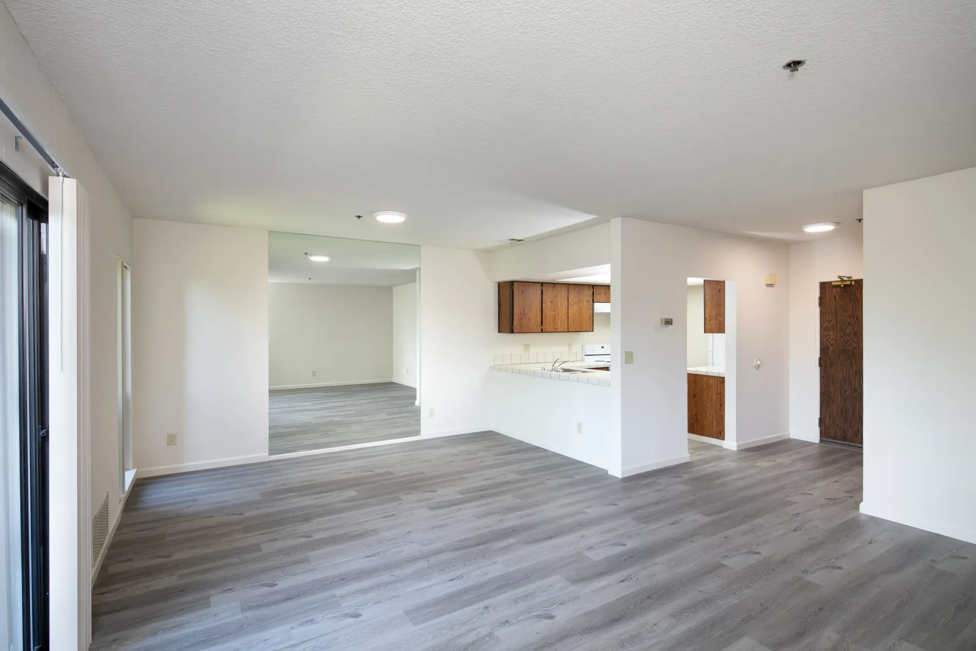 Spacious living area with wood-look flooring and a view into the kitchen.