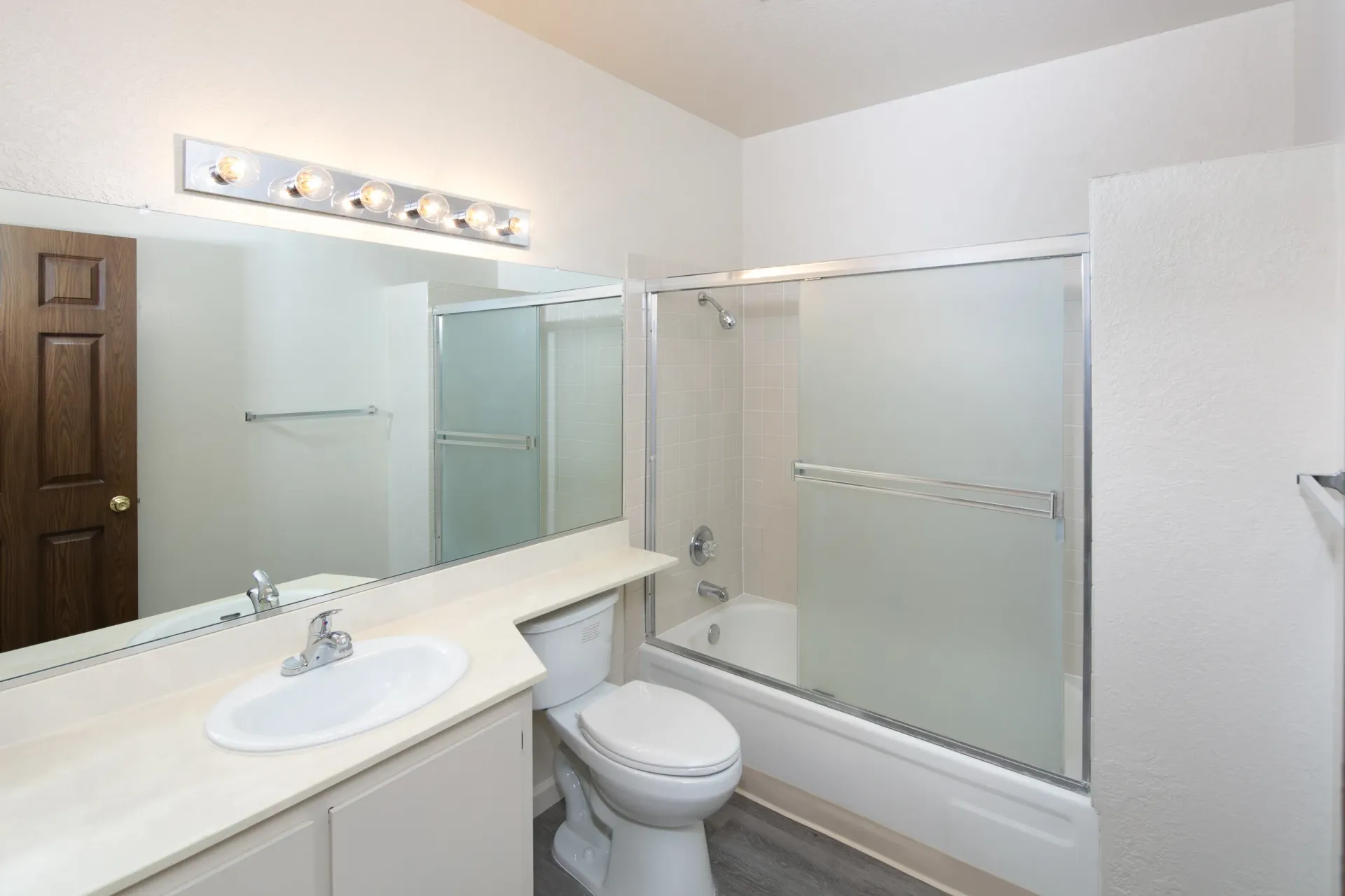 Modern bathroom with vanity, toilet, and bathtub with sliding glass door.
