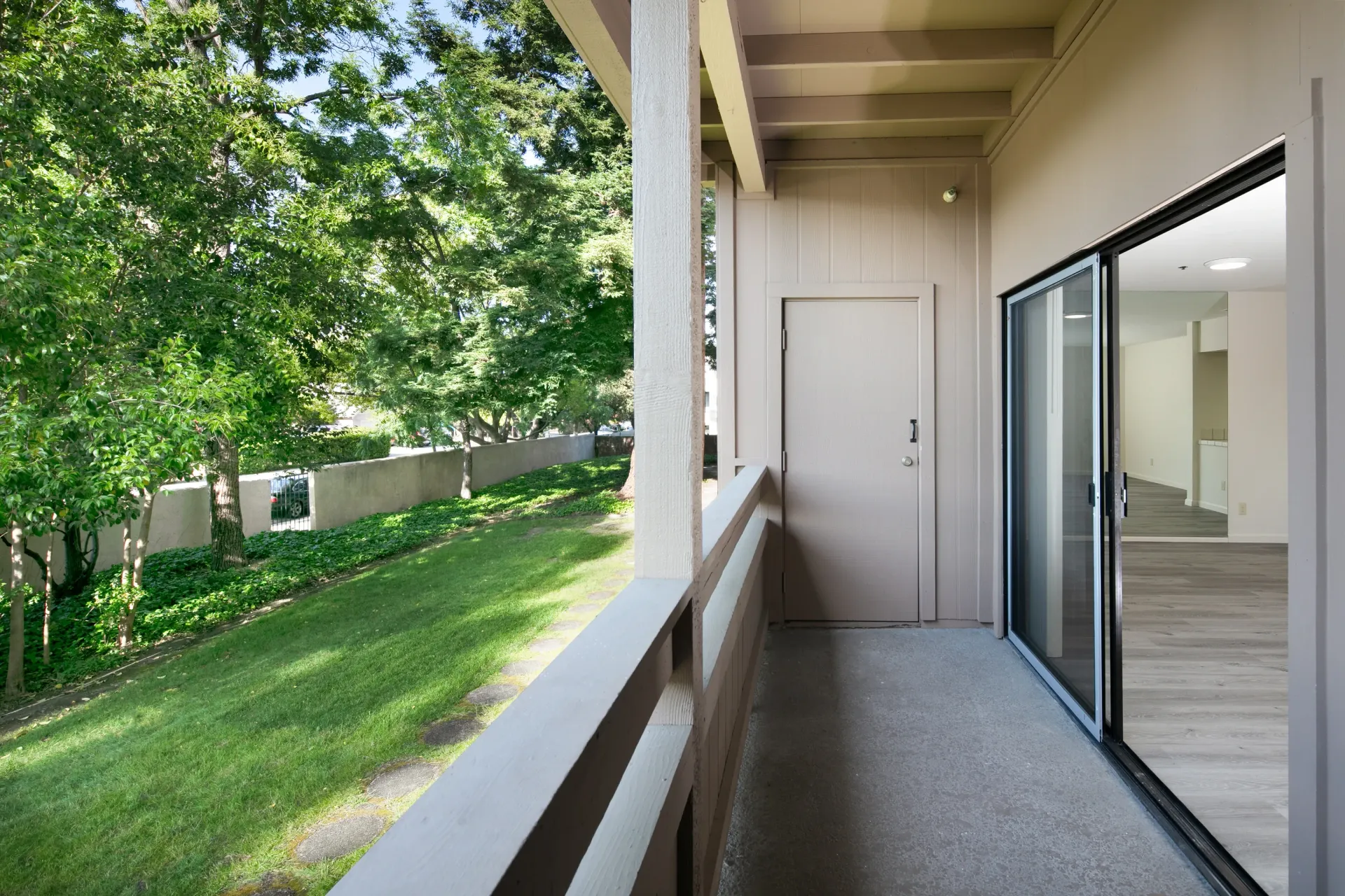 Balcony view of a grassy yard with trees and a wall, leading to an interior living space.