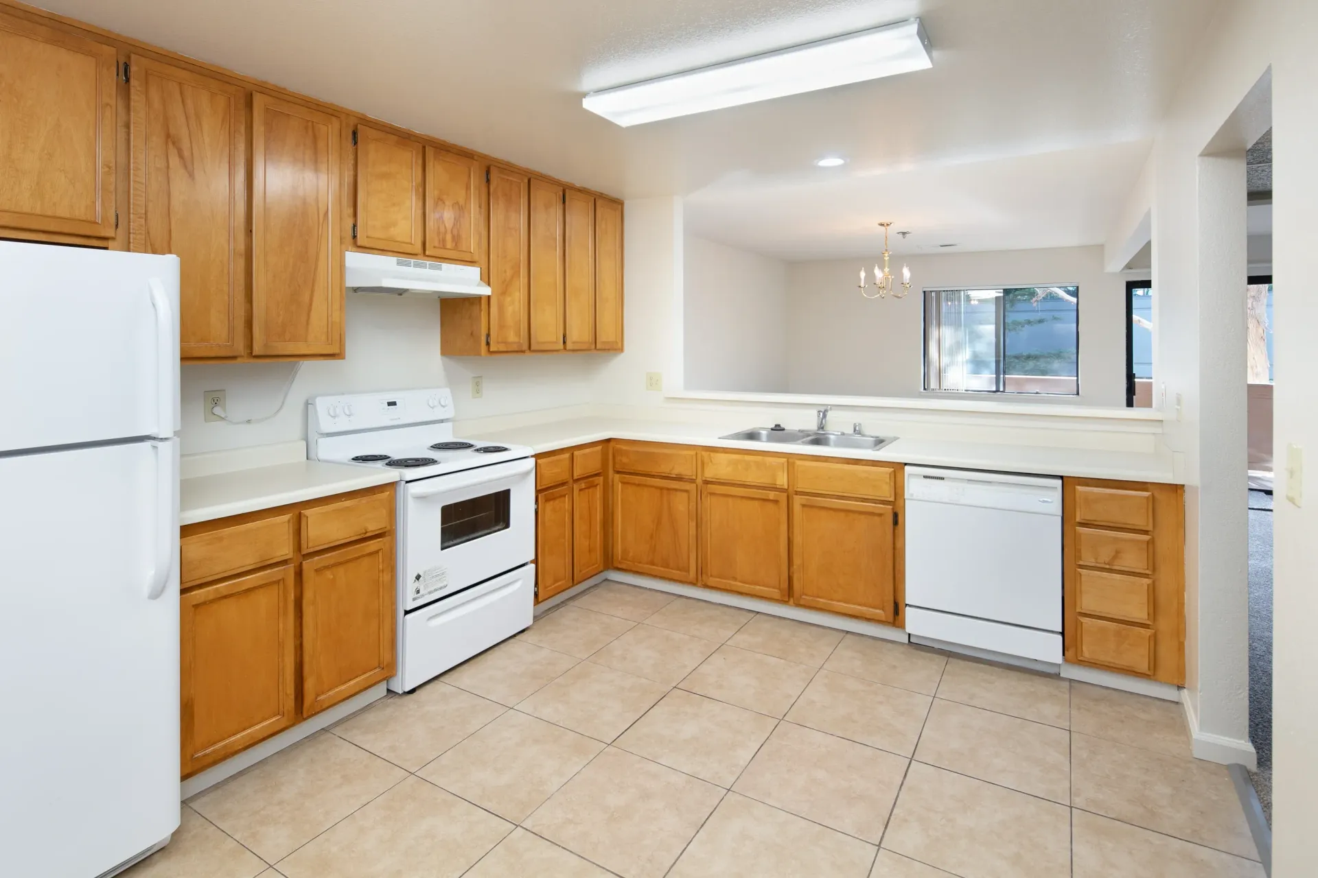 Kitchen with light wood cabinets, white appliances, and tiled flooring.