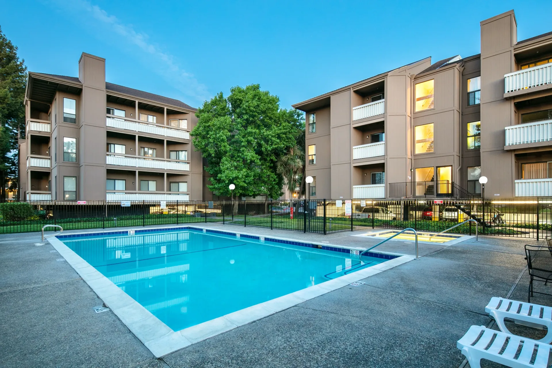 Outdoor swimming pool with lounge chairs and apartment buildings in the background.
