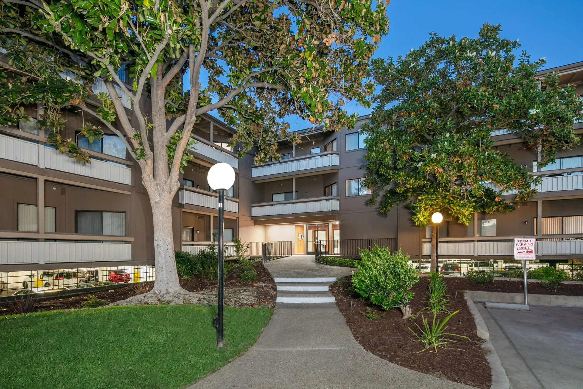 Exterior view of apartment building with entrance walkway and trees.