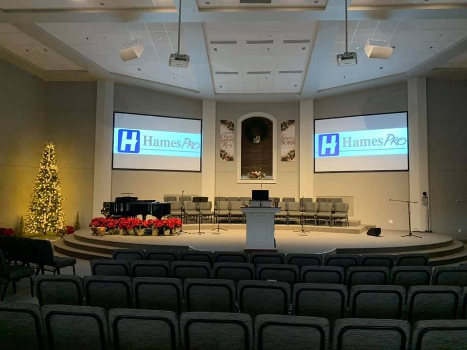 Empty auditorium with podium, projection screens, rows of chairs, and a lit Christmas tree on stage.