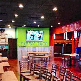 Inside a colorful restaurant, a Taffy Taco sign hangs above tables and chairs under ceiling lights.