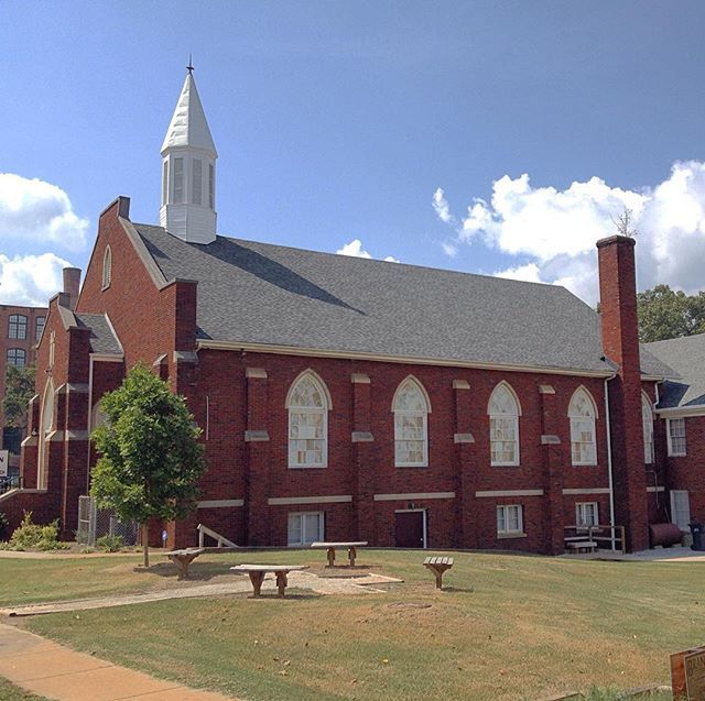 Red brick church with white steeple and arched windows on a sunny lawn