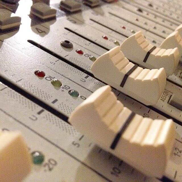 Close-up of an audio mixing console with white sliders and red indicator lights
