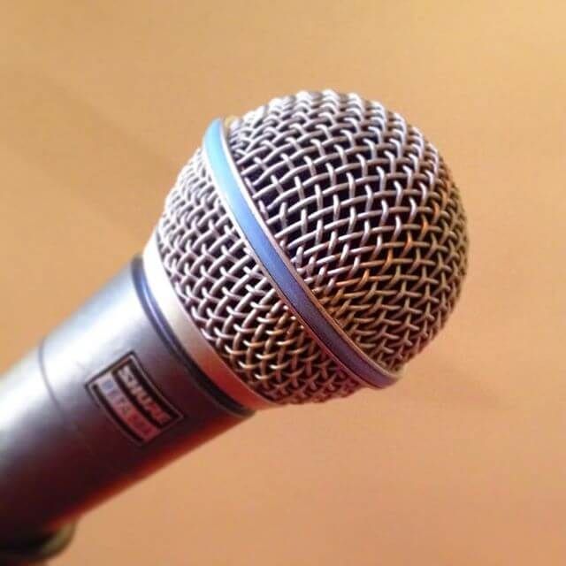 Close-up of a handheld microphone with a silver mesh grille against a warm orange background