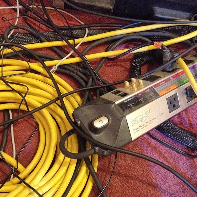 Tangled yellow and black cables around a silver power strip on a carpeted floor