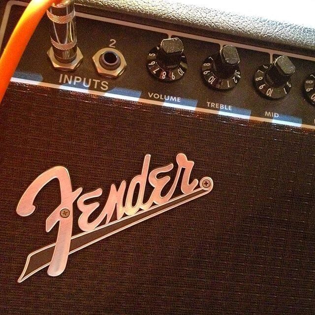 Close-up of a Fender guitar amplifier with black grille, orange trim, and control knobs.