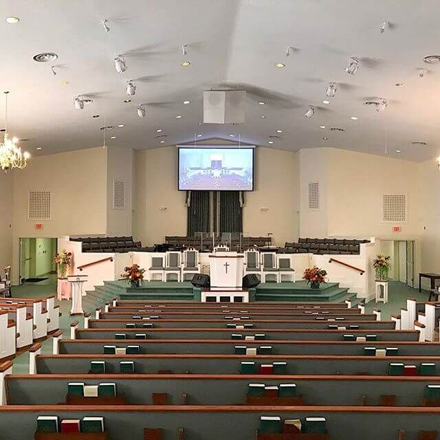 Empty church sanctuary with green pews, white walls, and a pulpit beneath a projection screen