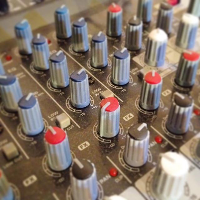 Close-up of an audio mixer with silver knobs, blue and red caps, and small red indicator lights