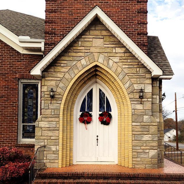 Brick church entrance with arched stone doorway and white double doors decorated with red wreaths